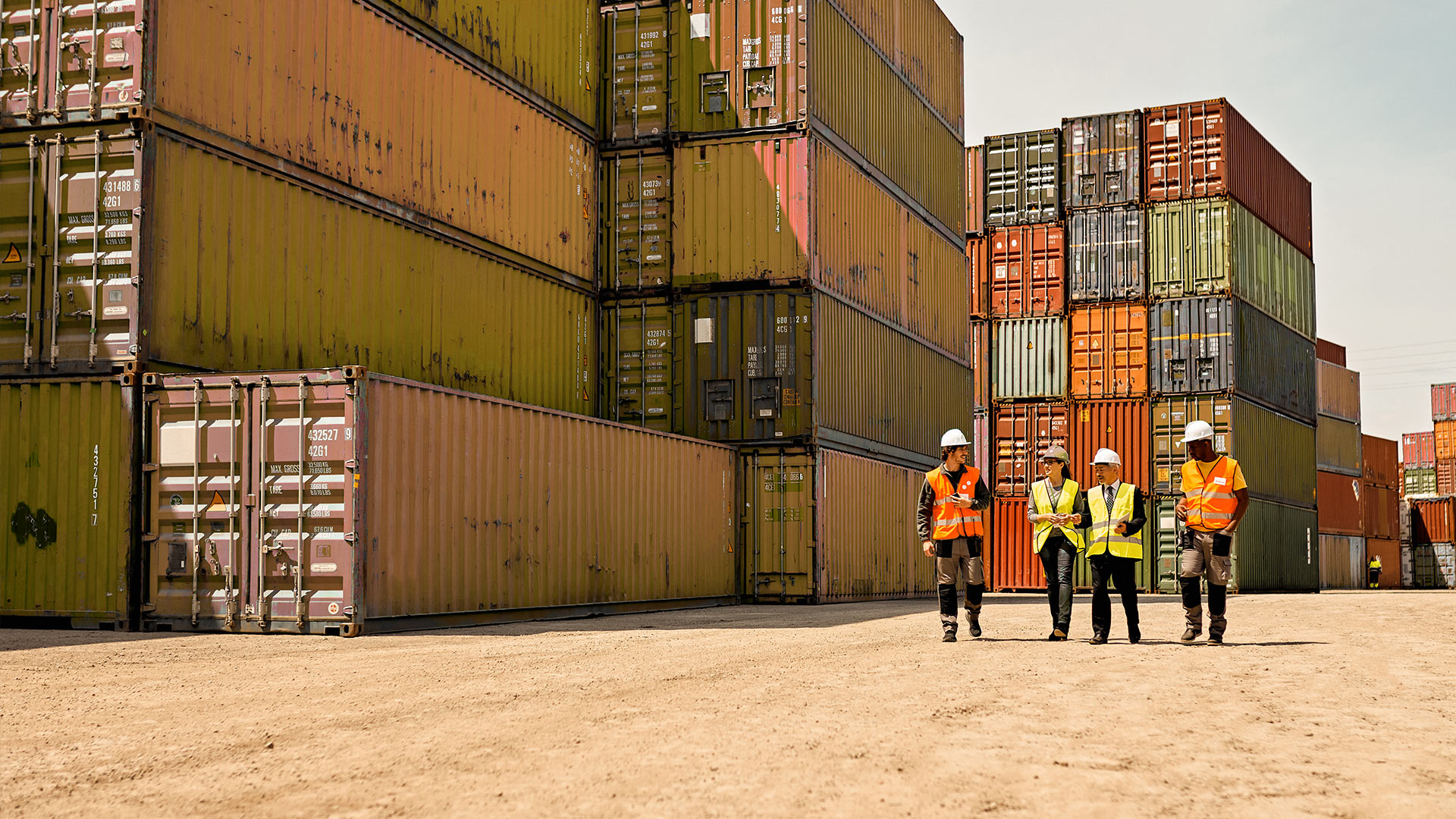 Vier Arbeiter gehen durch ein Containerterminal im Hafen