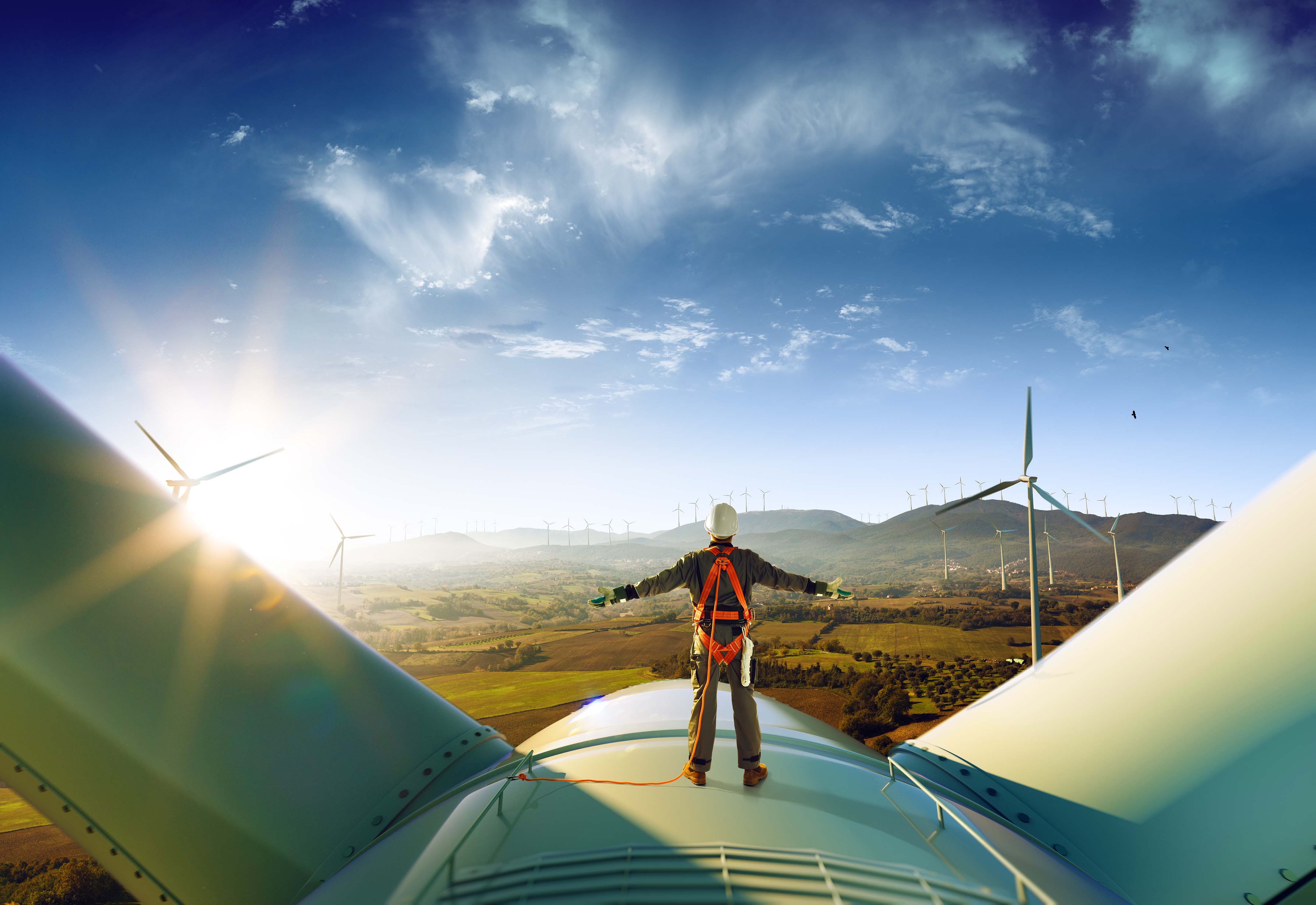 Bild: Arbeiter steht auf Windkraftanlage und schaut in Landschaft mit Windpark