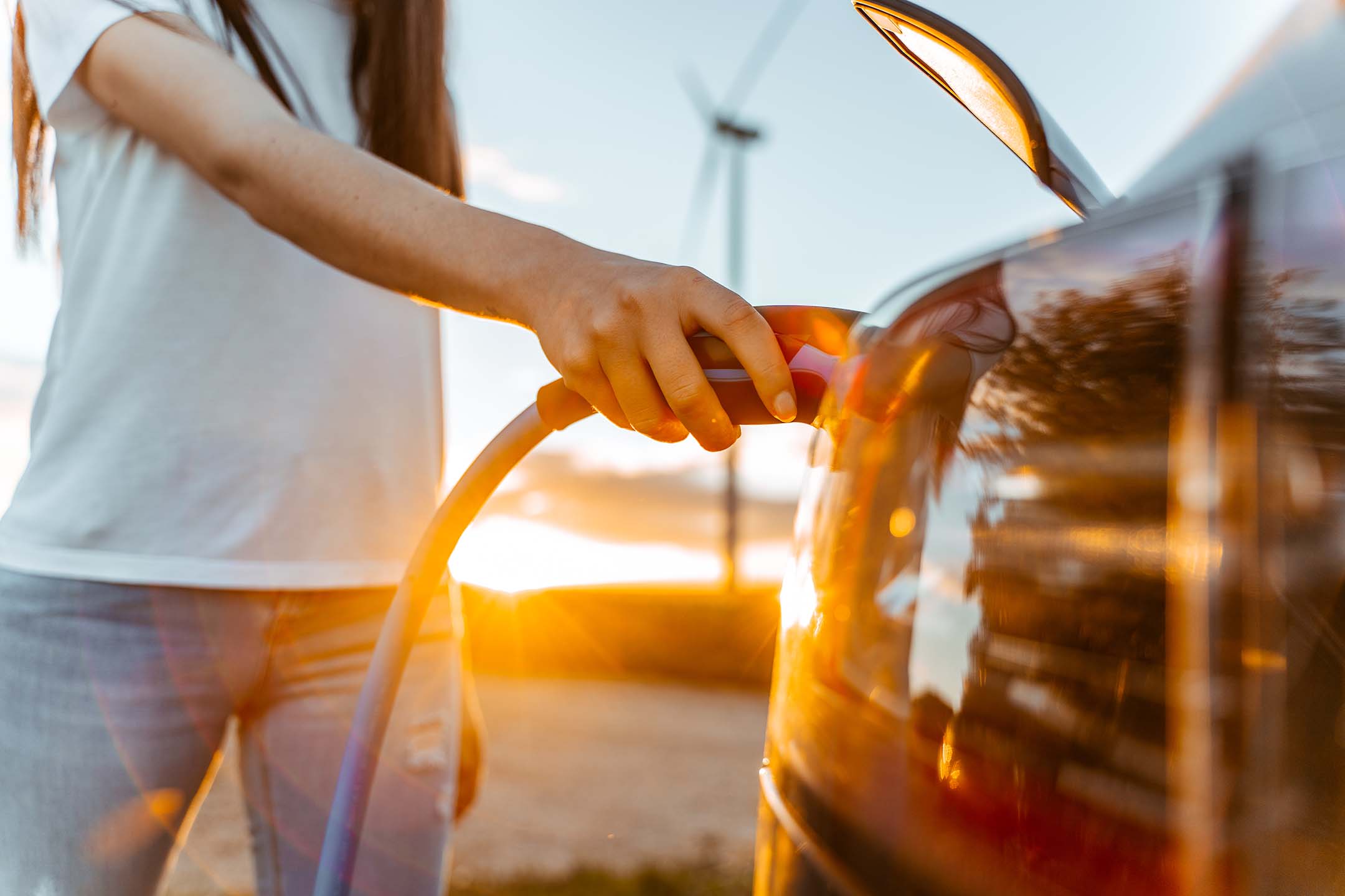 Image: Woman with charging cable in hand standing by an e-car