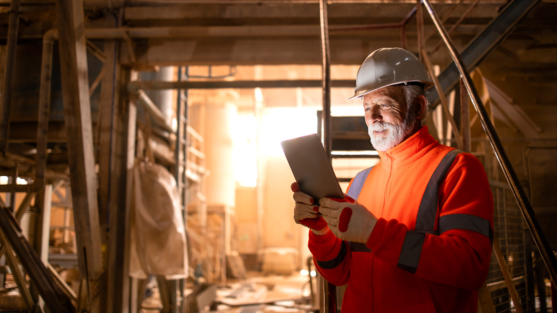 Ein Arbeiter steht in einer Fabrikhalle und schaut auf ein Tablet
