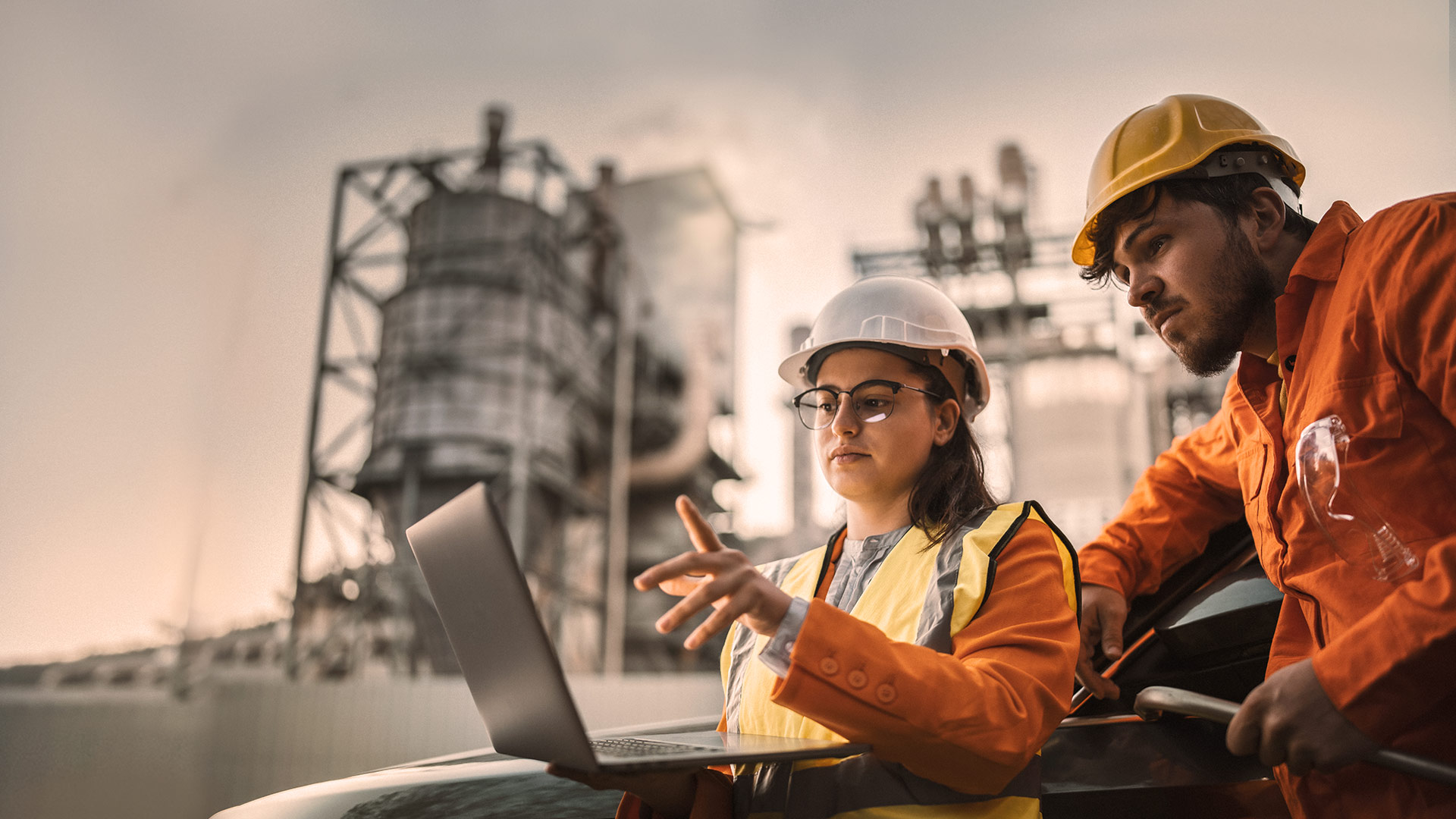 A man and a woman discuss content on a laptop on a factory site