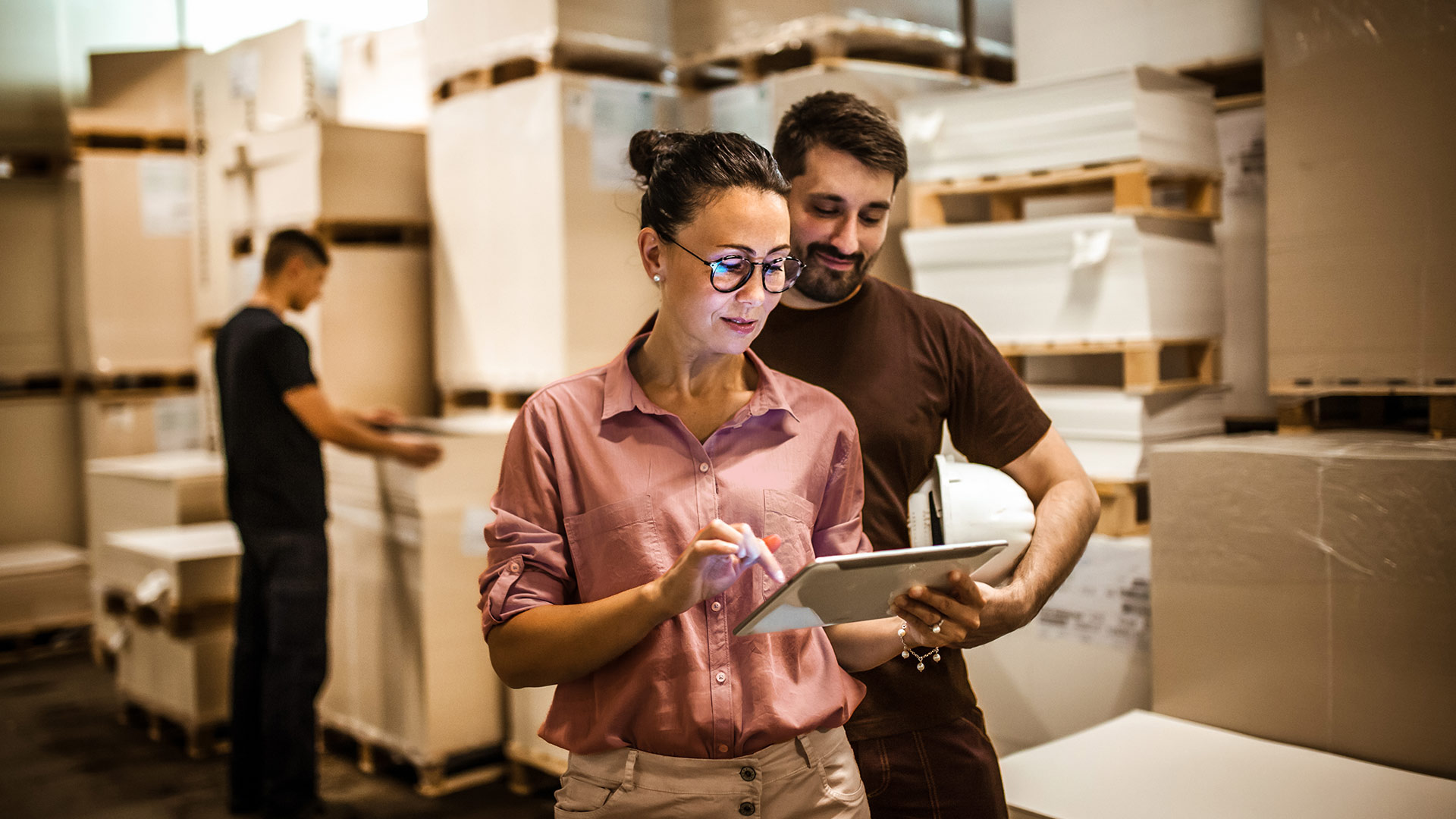 An employee shows a colleague something on a tablet in a warehouse.