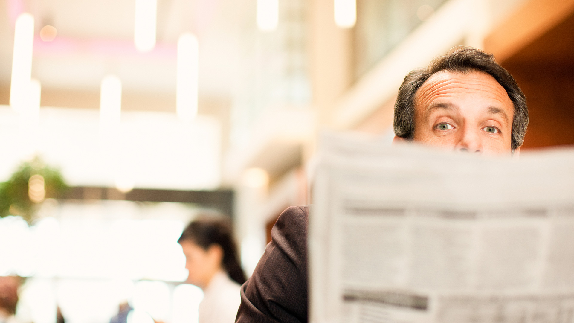 Ein Mann schaut hinter einer Zeitung hervor.